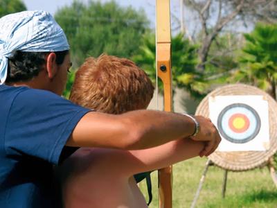 Zwei Personen beim Bogenschießen in einem grünen Außenbereich mit Zielscheibe.