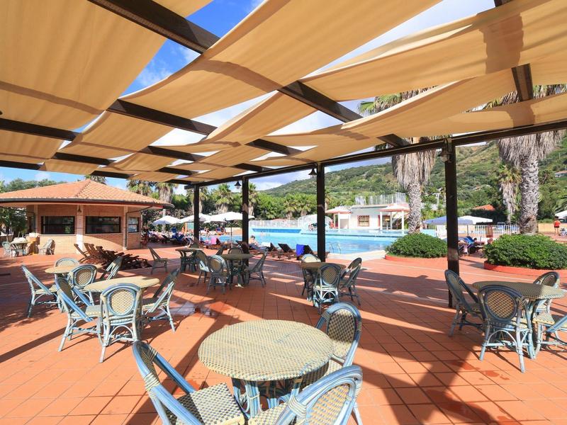 Terrasse couverte avec tables et chaises à côté d'une piscine d'hôtel dans un cadre ensoleillé.