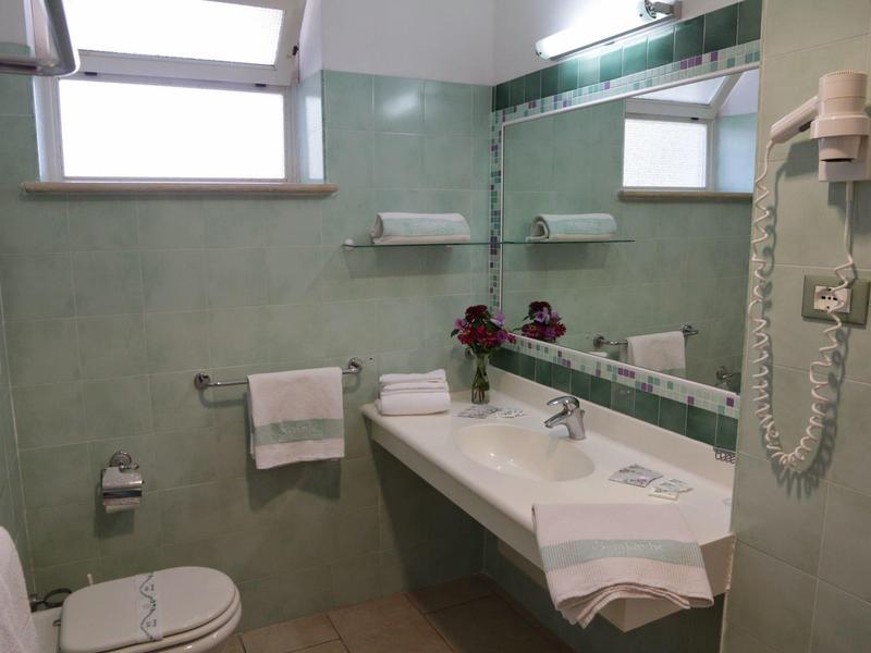 Salle de bain propre avec lavabo, miroir, toilette et sèche-cheveux sur des murs carrelés verdâtres.