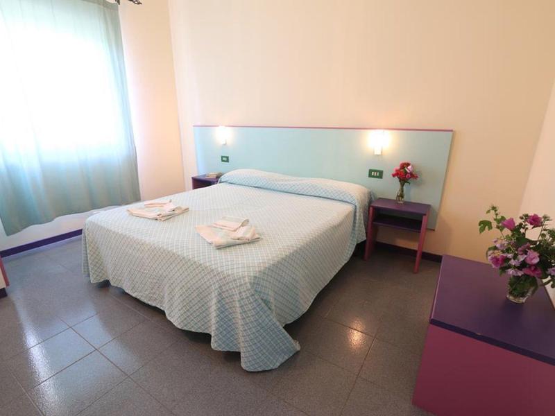 Une chambre d'hôtel simplement meublée avec lit double, tables de chevet et fenêtre avec rideau.