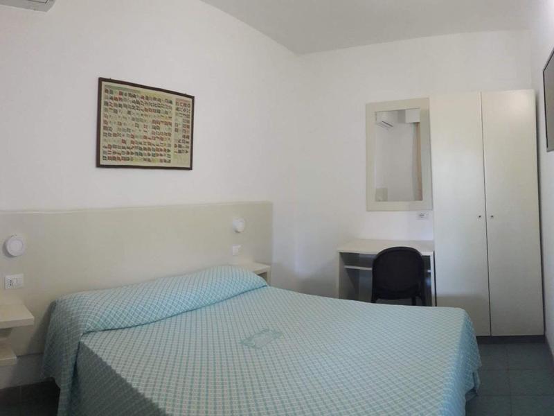 Chambre d'hôtel simple avec lit double, petit bureau, chaise et télévision murale.