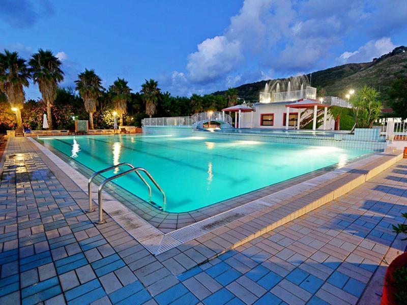 Piscine extérieure éclairée avec chaises longues et palmiers au crépuscule dans un complexe hôtelier.