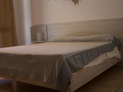 Schlichtes Schlafzimmer mit Doppelbett, hellen Holzmöbeln und braunen Vorhängen.