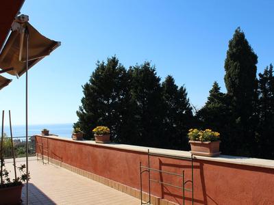 Terrassenbereich mit roten Mauern, Blumen in Töpfen und Blick auf Bäume und blauen Himmel.