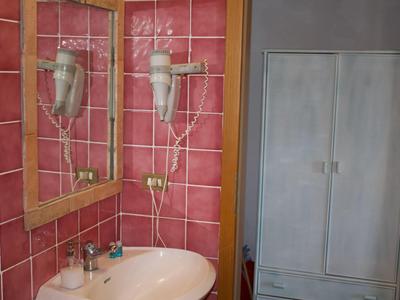 Ein Badezimmer mit rosa Kacheln, Waschbecken, Spiegel und Haartrockner an der Wand.