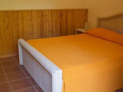 Schlichtes Schlafzimmer mit Doppelbett, orangenem Bettbezug, Holzverkleidung und Fliesenboden.