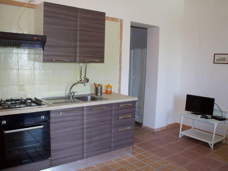 Kleine Küche mit grauen Schränken, Gasherd, Spüle und kleinem Fernseher auf weißem Tisch.