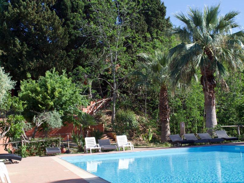 Klare Außenaufnahme eines blau gefüllten Pools, umgeben von Sonnenliegen und Palmen bei Sonnenschein.