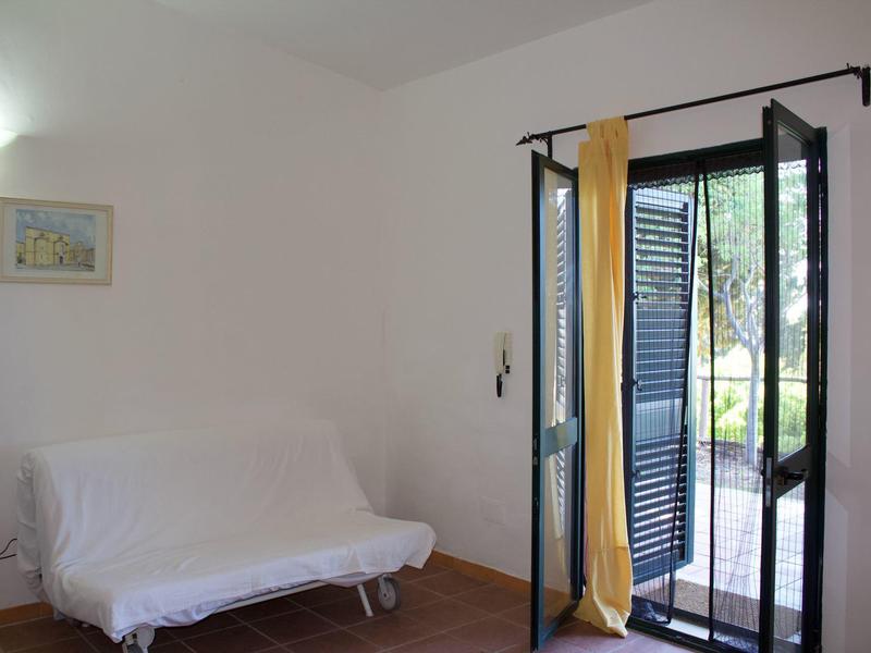 Hell eingerichtetes Zimmer mit weißem Sofa, braunem Boden und offener Glastür mit gelben Vorhängen.