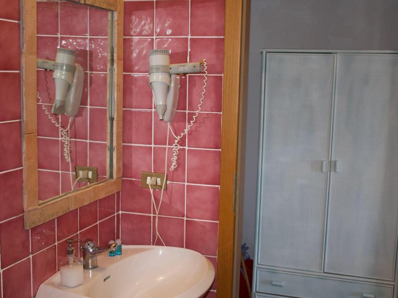 Ein Badezimmer mit rosa Kacheln, Waschbecken, Spiegel und Haartrockner an der Wand.