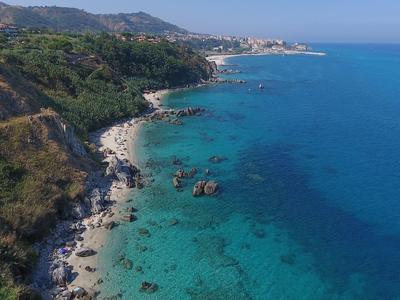 Côte avec eau bleue claire, rochers et collines verdoyantes en arrière-plan.