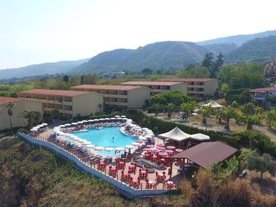 Hotelanlage mit einem Pool auf einem Hügel mit umliegenden Bergen und Gebäuden.
