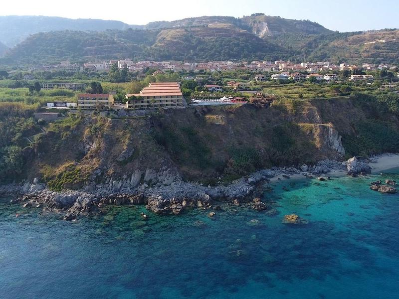Falaises avec eau bleue claire et bâtiments au sommet d'une côte verte avec des collines en arrière-plan.