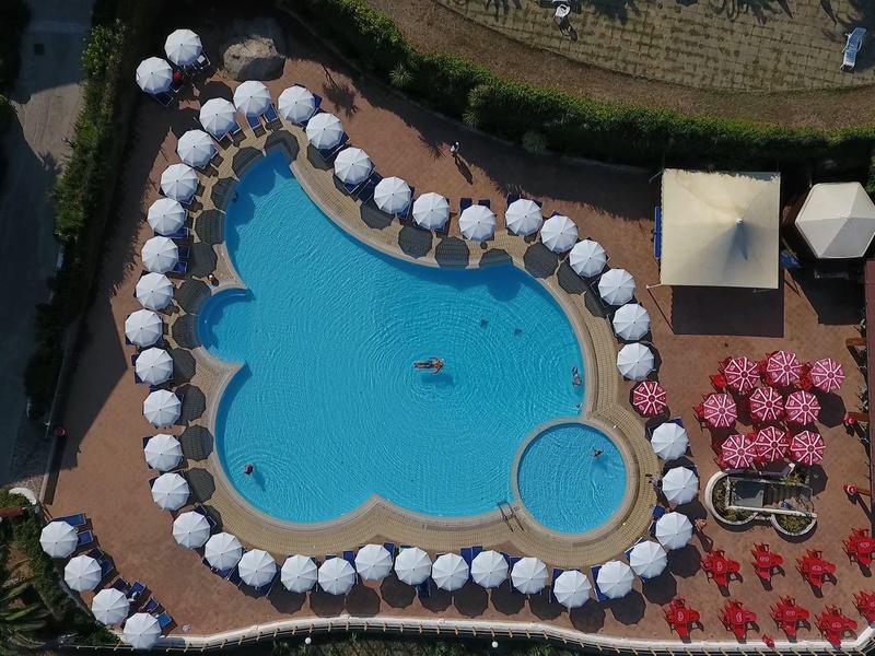 Grande piscine bleue avec de nombreux parasols blancs et chaises longues sur une terrasse d'hôtel.