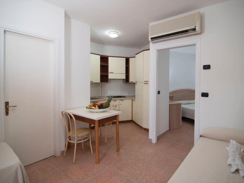 Logement compact avec kitchenette, petite table, chaises et vue sur la chambre.