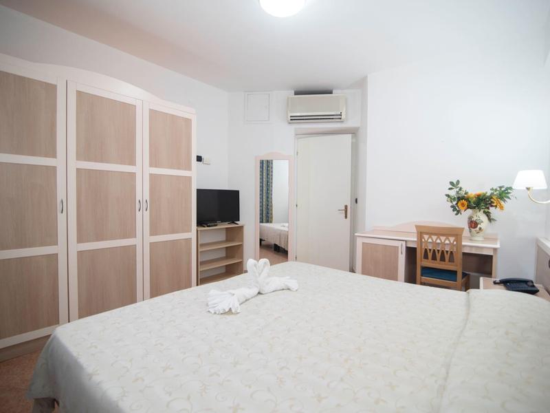 Chambre lumineuse avec lit double, armoire, bureau et télévision dans un style moderne.