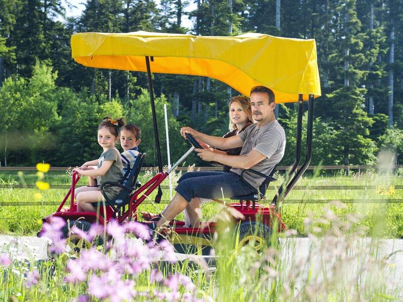 Twee volwassenen en twee kinderen rijden op een vierpersoonsfiets met een geel dak.