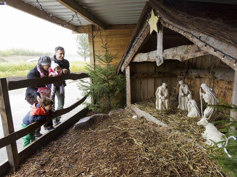 Familie bekijkt een buiten kerststal omringd door hout en stro.