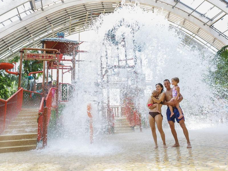Familie met kinderen speelt onder een grote waterval in een tropisch waterpark.