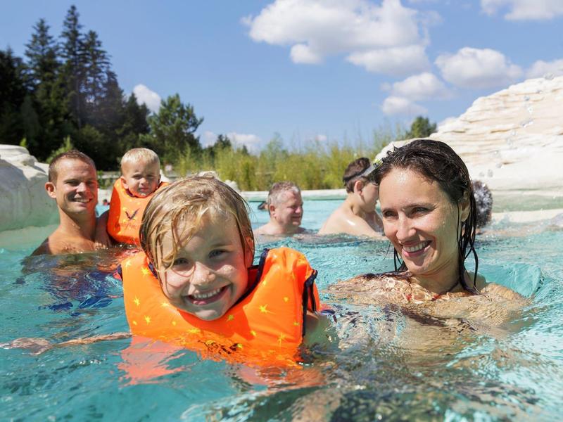 Familie met kinderen in een zwembad omgeven door rotsen op een zonnige dag.