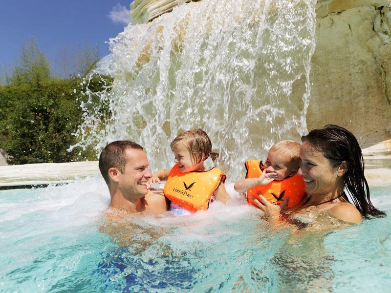 Familie met jonge kinderen in zwemvesten in een zwembad voor een waterval.
