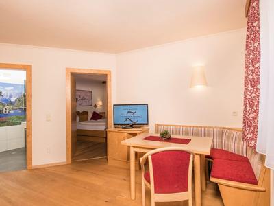 Heller Wohnraum mit Holzboden, rotem Sitzbereich, Tisch und Blick zu zwei offenen Türen.