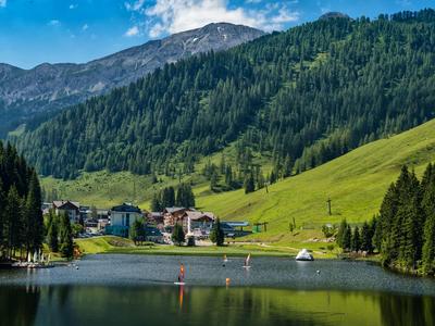 Bergsee mit klarer Wasseroberfläche, umgeben von grünen Wäldern und grasbewachsenen Hängen.