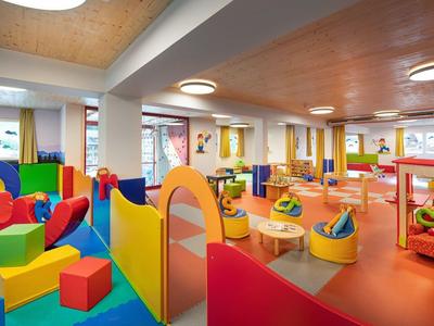 Bunter Kindergartenraum mit Klettergerüsten, Sitzkissen und Spielmatten, viel Licht und fröhlicher Atmosphäre.