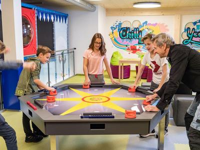 Fünf Jugendliche spielen an einem modernen Airhockey-Tisch in einem farbenfrohen Raum.