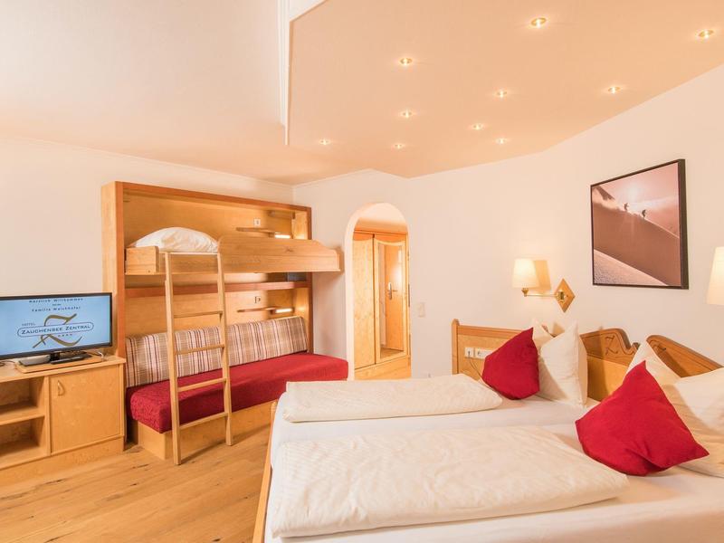 Helles Schlafzimmer mit Doppelbett, Stockbett, Holzmöbeln und roten Kissen.