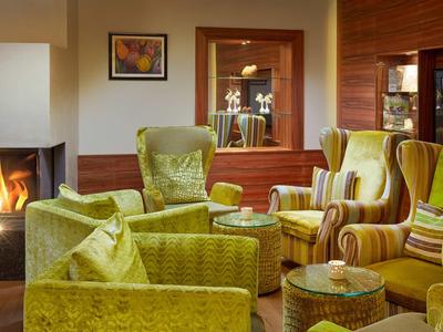 Gemütliche Lounge mit grünen Sesseln, Kamin und warmem Holzdekor in einem Hotel.