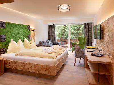 Gemütliches Hotelzimmer mit Holzvertäfelungen, großem Bett, Sofa und Fenster mit Blick ins Grüne.