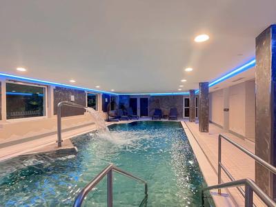 Moderner Innenpool mit blauen LED-Lichtern, Wasserfontäne und Metallgeländern in hellem Raum.