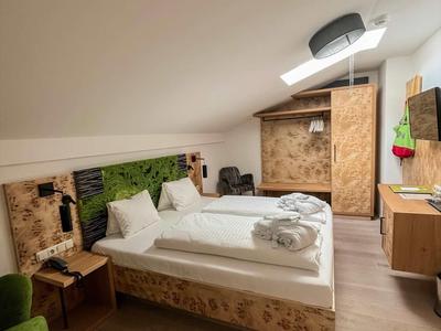 Hell eingerichtetes Schlafzimmer mit Holzverkleidung, Doppelbett, grünem Sessel und moderner Beleuchtung.