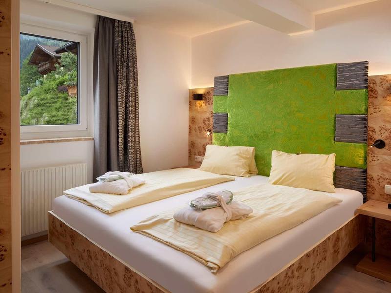 Gemütliches Schlafzimmer mit Holzverkleidung, grünem Kopfteil und viel natürlichem Licht.