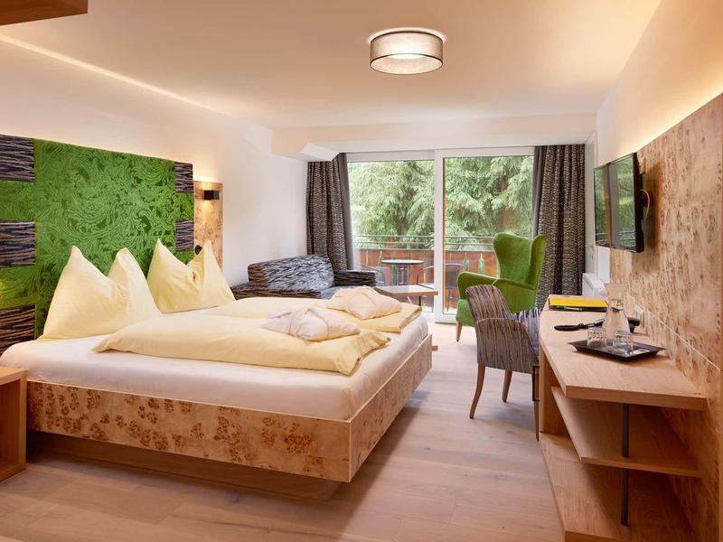 Gemütliches Hotelzimmer mit Holzvertäfelungen, großem Bett, Sofa und Fenster mit Blick ins Grüne.