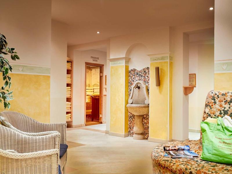 Helles Wohnzimmer mit gelb-weiß gestrichenen Wänden, Korbstühlen und Sofa mit Blumenmuster.