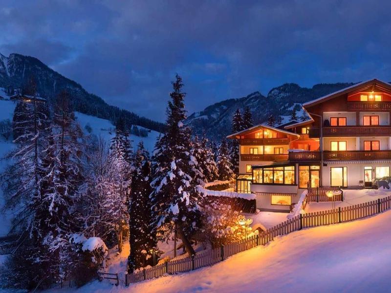 Ein beleuchtetes Chalet in schneebedeckter Berglandschaft bei Abenddämmerung.