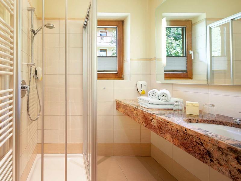 Helles Badezimmer mit Dusche, großem Marmorwaschtisch, zwei Fenstern und Handtüchern.