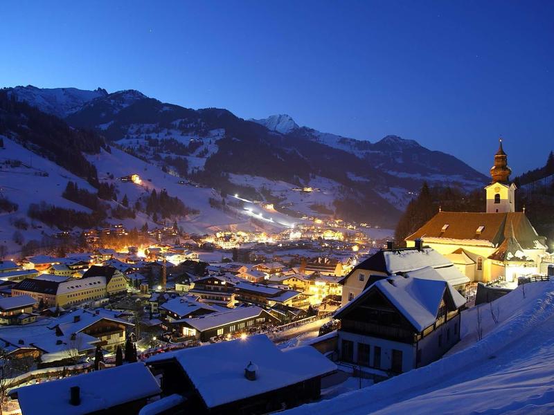 Winterliches Bergdorf bei Dämmerung mit schneebedeckten Häusern und beleuchteter Kirche.
