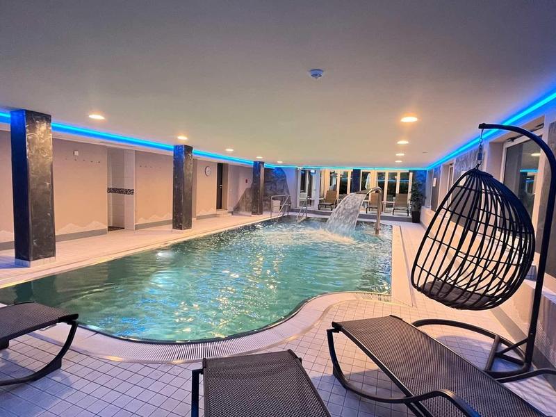 Innenpool mit blauer LED-Beleuchtung, Liegestühlen und einer hängenden Korbschaukel.