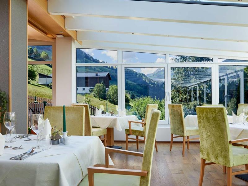 Helles Restaurant mit grünen Stühlen und Panoramafenstern mit Bergblick.