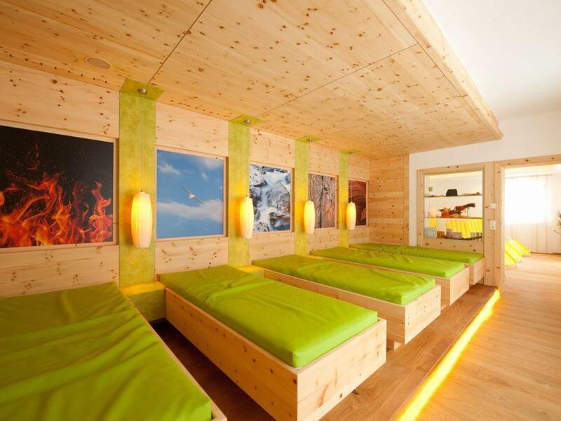 Hell eingerichtetes Schlafzimmer mit vier Holzbettgestellen und grüner Bettwäsche, Wandbilder und Holzdecken.