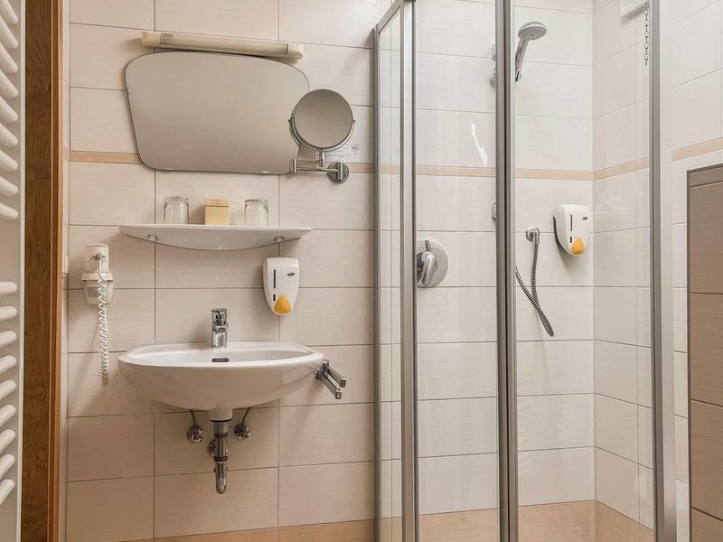 Kleines Badezimmer mit runder Duschkabine, Wandspiegel, weißem Waschbecken und beige Fliesen.