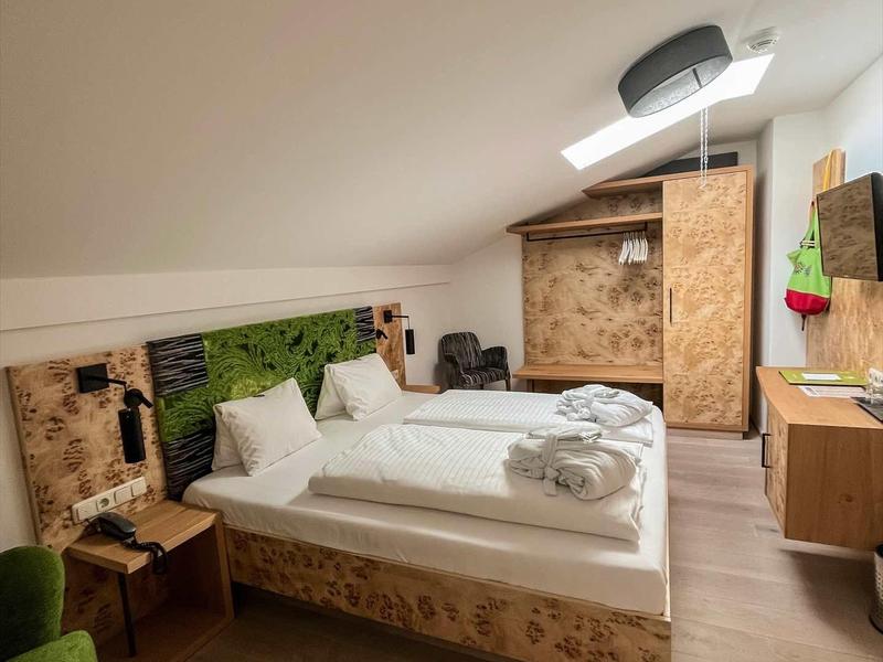 Hell eingerichtetes Schlafzimmer mit Holzverkleidung, Doppelbett, grünem Sessel und moderner Beleuchtung.