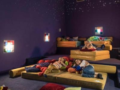 Kinder liegen auf bunten Matratzen in einem abgedunkelten Raum mit Sternenlichtprojektoren.