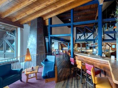 Moderne Hotelbar mit Holzdecken, bunten Sesseln und großen Fenstern