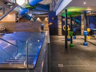 Innenbereich eines modernen Hallenbads mit Wasserrutsche und Fitnessgeräten.