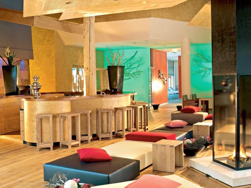 Modern eingerichteter Hotel-Loungebereich mit Sitzkissen, Hockern und Kamin.