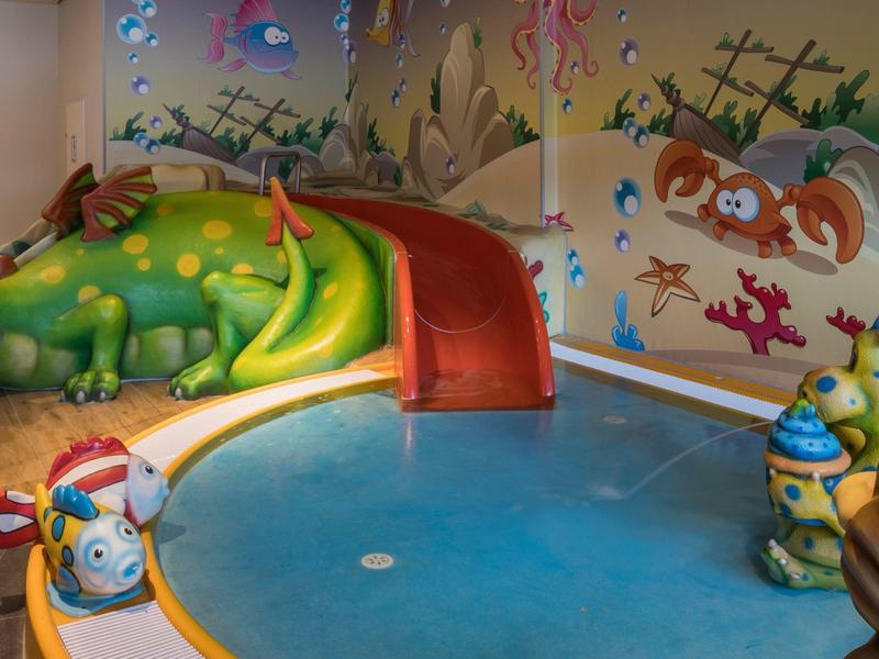 Bunter Innenpool mit einer Drachenrutsche und Wandmalereien mit Meeres- und Waldtieren.